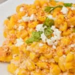 A plate of Mexican Street Corn Casserole salad topped with crumbled cheese, chili powder, and fresh cilantro, with a fork in the background.