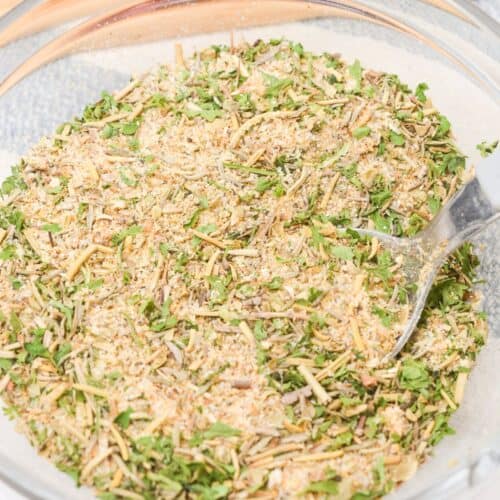 A clear glass bowl filled with a mixed dry herb and spice pot roast seasoning recipe blend, with a spoon partially visible on the right side.