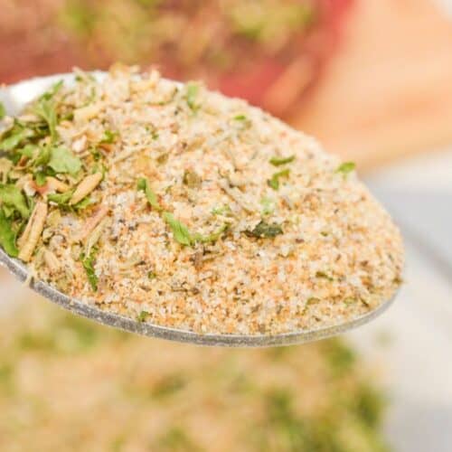 A close-up of a spoon holding a mixed dry Pot Roast Seasoning recipe with herbs and spices, above a bowl containing more of the mixture.