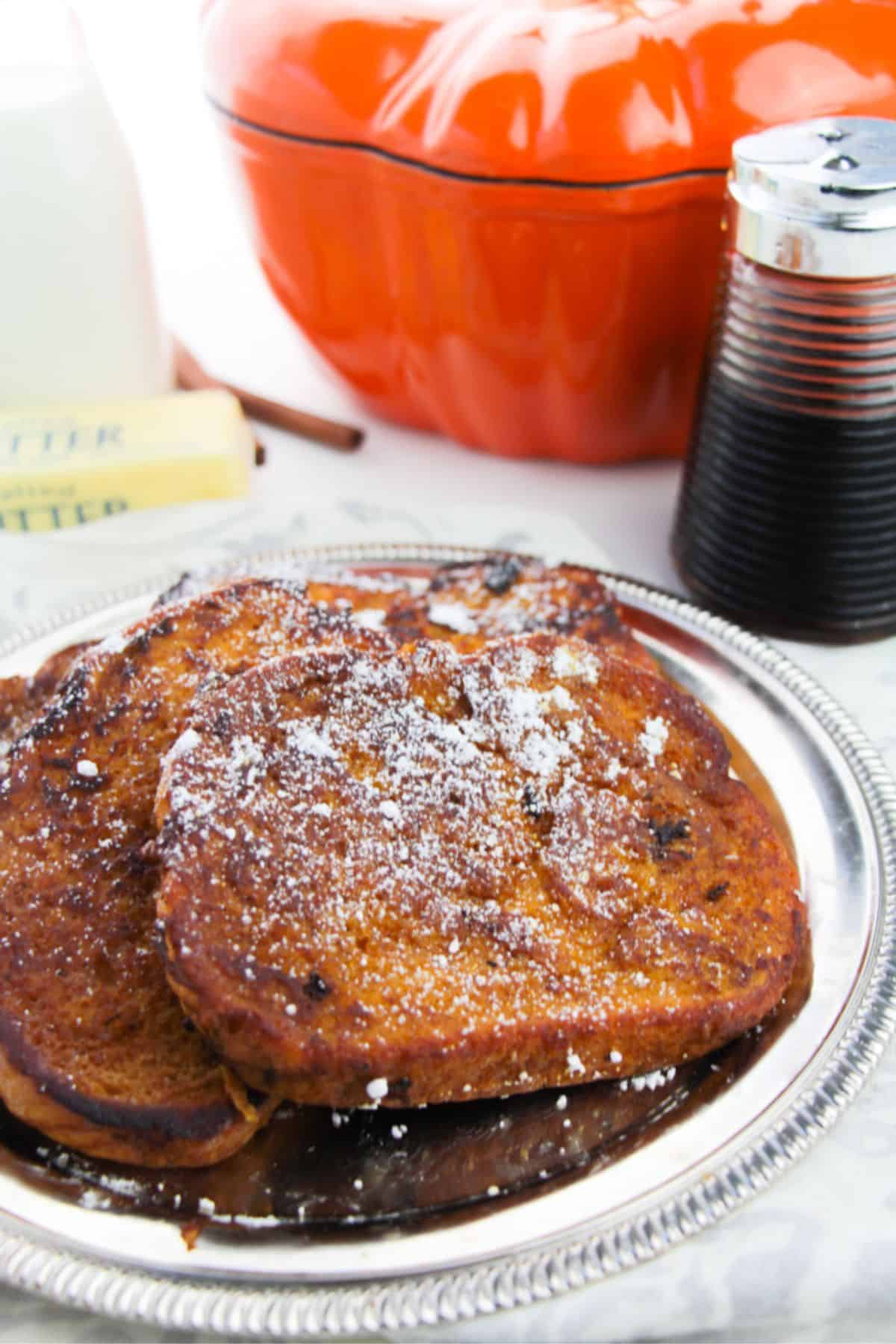 Breakfast dusted with powdered sugar on a silver plate, with syrup, butter, milk, and an orange dish in the background.