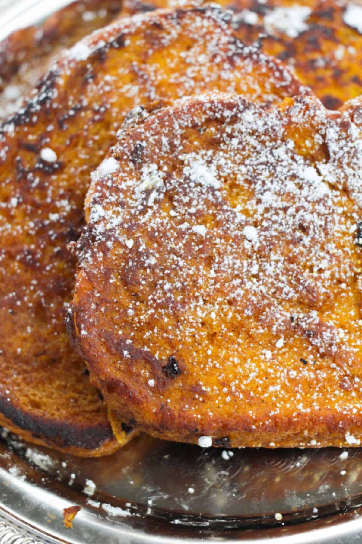 Close-up of Pumpkin Pie Spice French Toast slices dusted with powdered sugar on a silver plate.