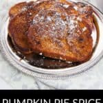 A plate of Pumpkin Pie Spice French Toast dusted with powdered sugar sits on a silver tray, highlighting the cozy flavors of fall. A butter stick and orange bowl in the background complete this inviting breakfast scene.