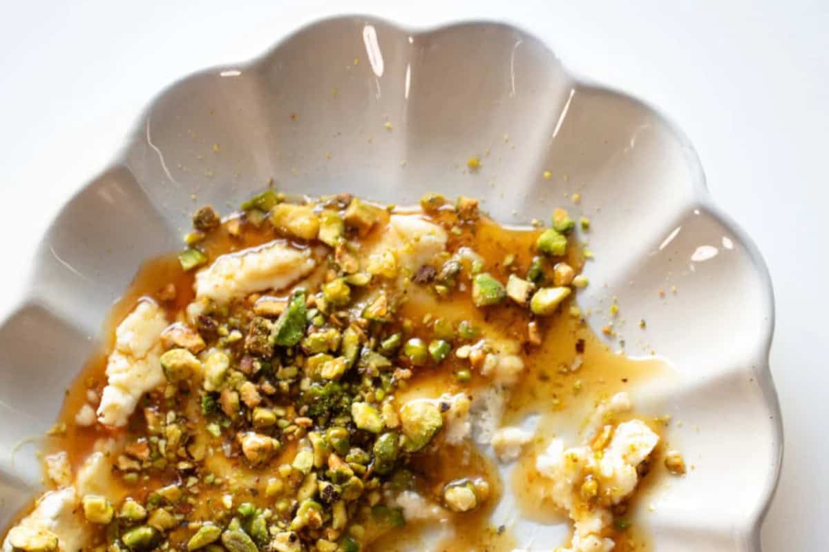 A scalloped white plate with partially eaten Boursin cheese topped with chopped pistachios and hot honey.