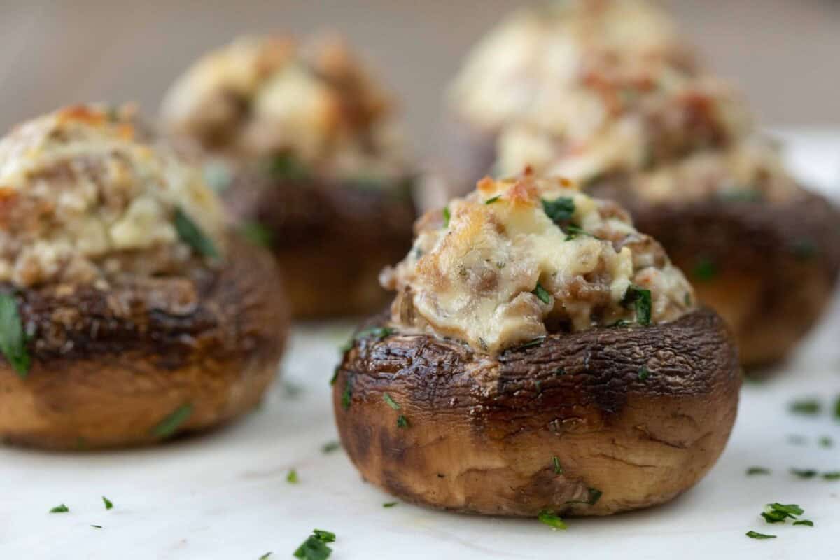 Close-up of stuffed mushrooms filled with a creamy Boursin cheese and sausage mixture placed on a white surface.
