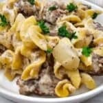 A plate of creamy beef and noodle casserole garnished with parsley, placed on a white surface with a yellow-striped towel in the background. Text reads: "Casserole recipes everyone loves.