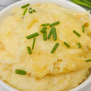 A bowl of creamy Cheesy Mashed Potatoes garnished with chopped chives.
