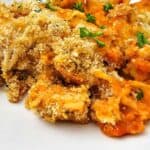 Chicken Parmesan Casserole baked pasta topped with golden breadcrumbs and garnished with chopped parsley on a white plate.