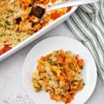 A golden breadcrumb topping, served on a white plate beside a casserole dish and garnished with chopped herbs.