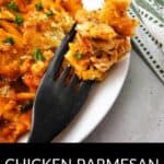 A white plate with Chicken Parmesan Casserole, a black fork holding a bite, and a green-striped napkin beside the plate.