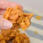 A hand holding a treat, with more clusters on a plate in the background.