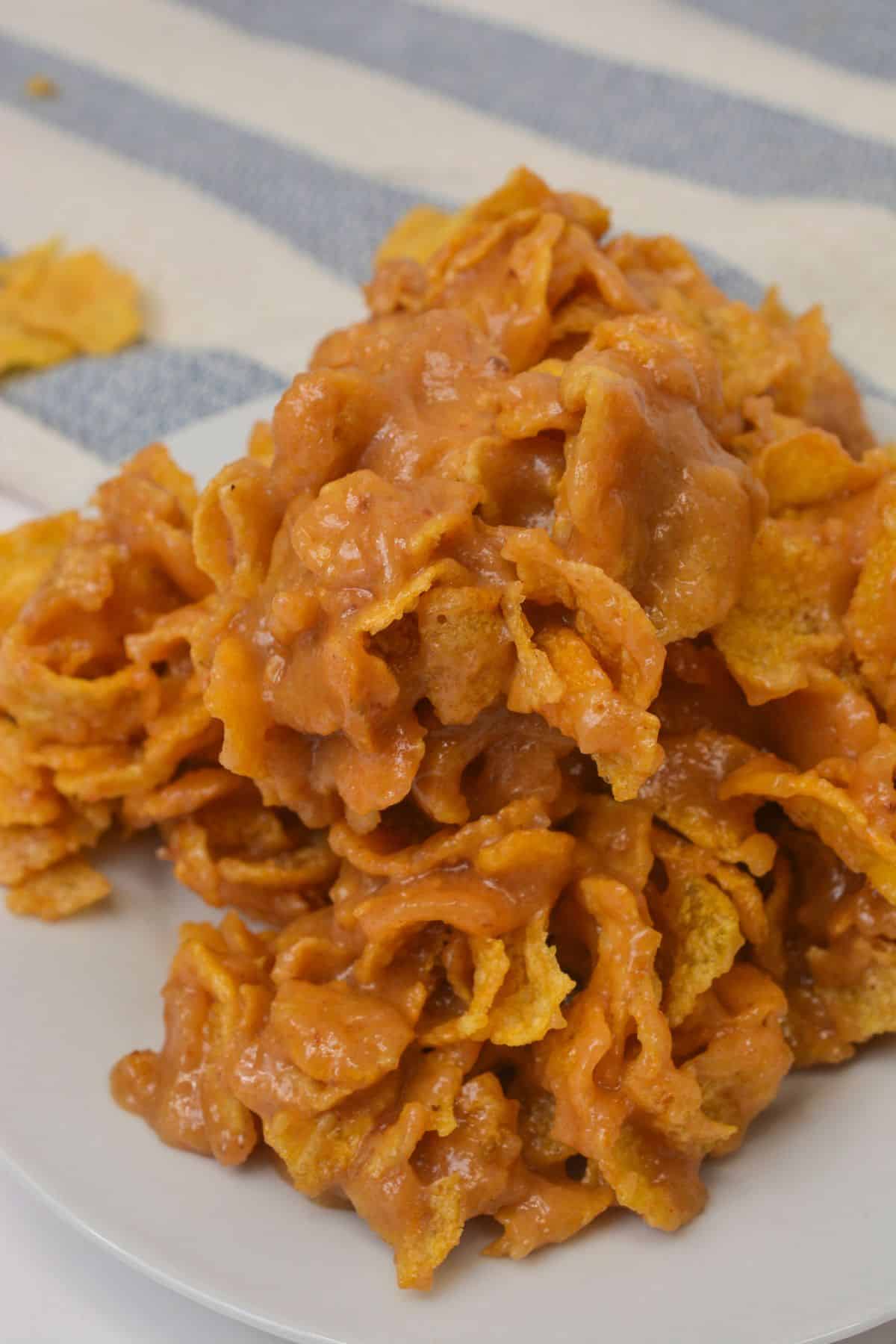 A close-up of a stack of caramel-coated Cornflake Cookies clusters on a white plate, with a striped fabric in the background.