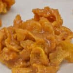 A close-up of Cornflake Cookies—a cluster of cornflakes coated in a caramel-like mixture, resting on a sheet of parchment paper.