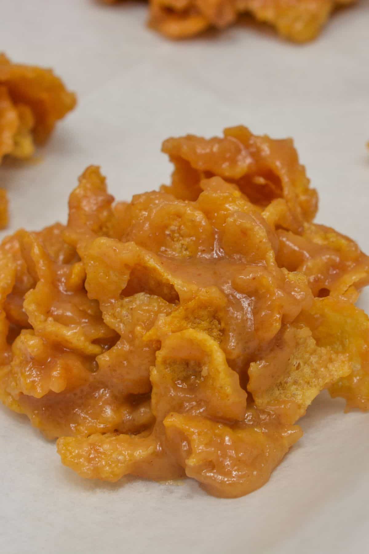 A close-up of Cornflake Cookies—a cluster of cornflakes coated in a caramel-like mixture, resting on a sheet of parchment paper.