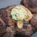 A cooked steak topped with the recipe, served on a gray plate.