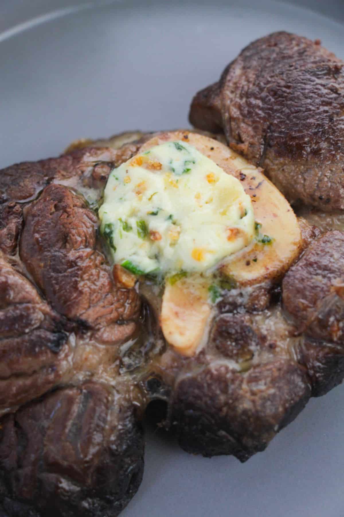 A cooked steak topped with the recipe, served on a gray plate.