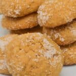 A plate of round, golden-brown Ginger Molasses Cookies coated with granulated sugar, stacked and arranged closely together.