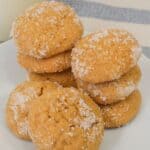 A white plate with stacks of round, golden Ginger Molasses Cookies coated in granulated sugar, set in front of a blue and white striped cloth.