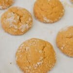 Round treats that are sugar-coated and freshly baked, rest on a sheet of parchment paper with slightly cracked surfaces.