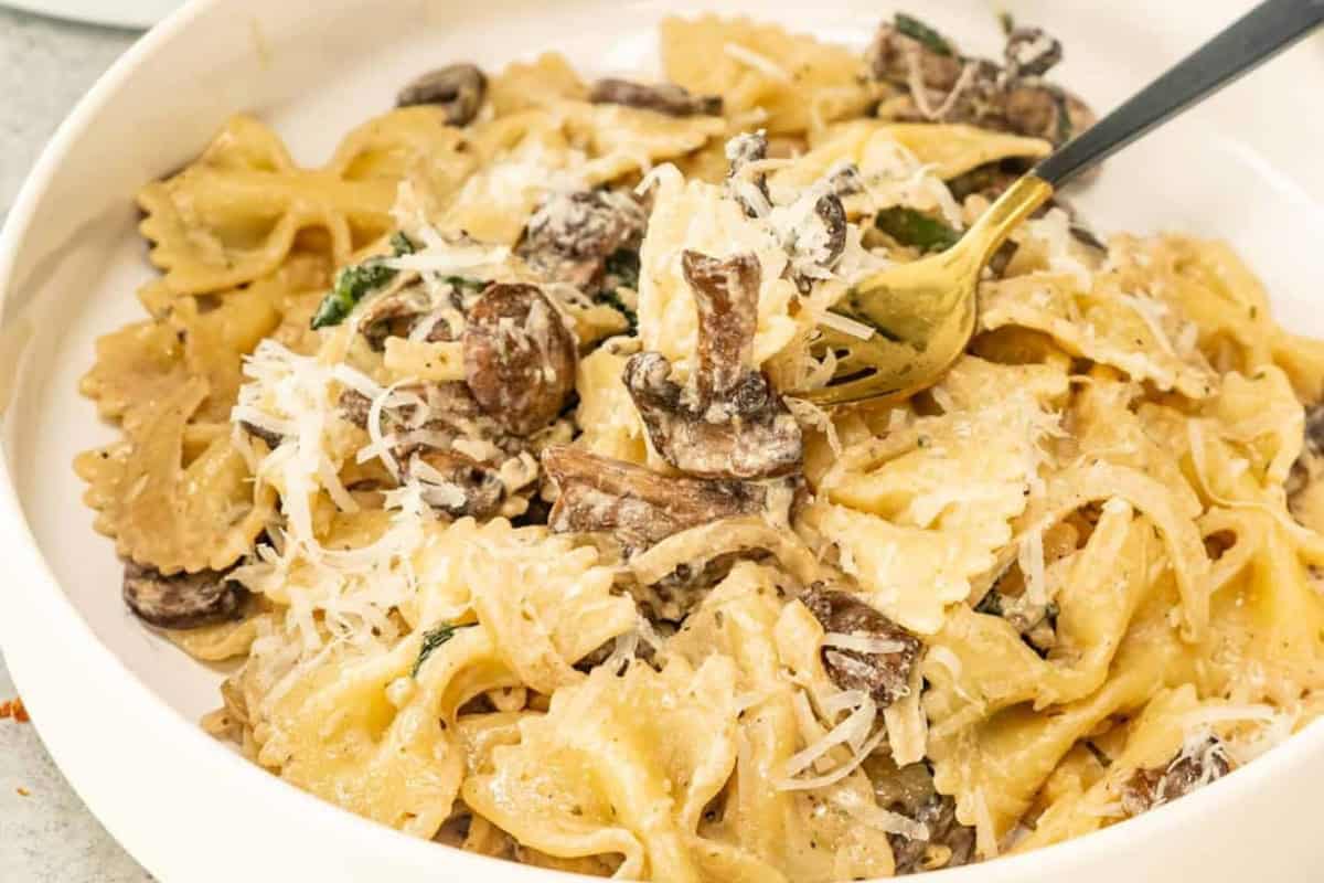 A plate of bow tie pasta with creamy  Boursin sauce, mushrooms, greens, and grated cheese. A fork rests invitingly in the dish.