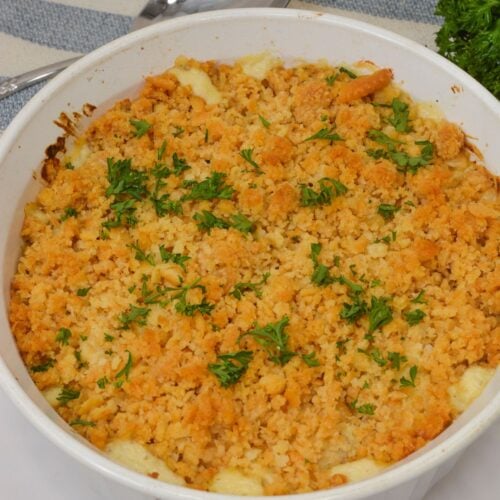 A white casserole dish filled with Ritz Cracker Chicken Casserole, baked to perfection and topped with golden brown breadcrumbs, garnished with chopped parsley.