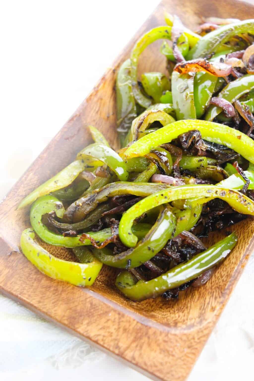 Sautéed Onions and Peppers—fresh green bell pepper and onion strips—served on a rectangular wooden plate.