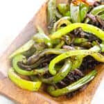 Sautéed Onions and Peppers—fresh green bell pepper and onion strips—served on a rectangular wooden plate.