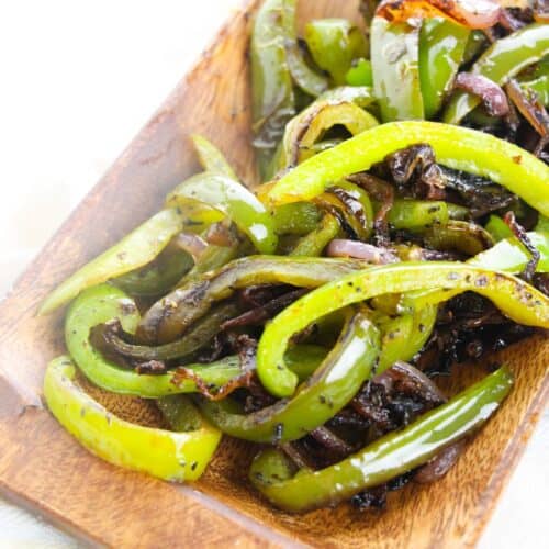 Sautéed Onions and Peppers—fresh green bell pepper and onion strips—served on a rectangular wooden plate.