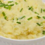 A white bowl filled with Boursin Mashed Potatoes, garnished with chopped green chives.