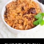A white bowl filled with flavorful Chipotle Slow Cooker Chicken, shredded and garnished with a sprig of cilantro, sits atop a white cloth.