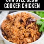 A white bowl filled with flavorful Chipotle Slow Cooker Chicken, garnished with a fresh cilantro sprig, sits on a light surface.