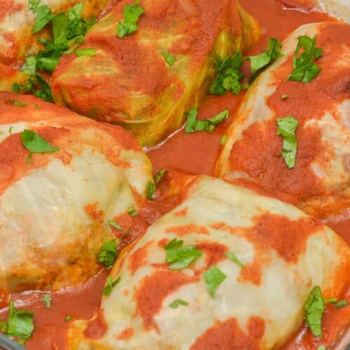 Five Easy Stuffed Cabbage Rolls topped with tomato sauce and garnished with chopped parsley are arranged in a glass baking dish.