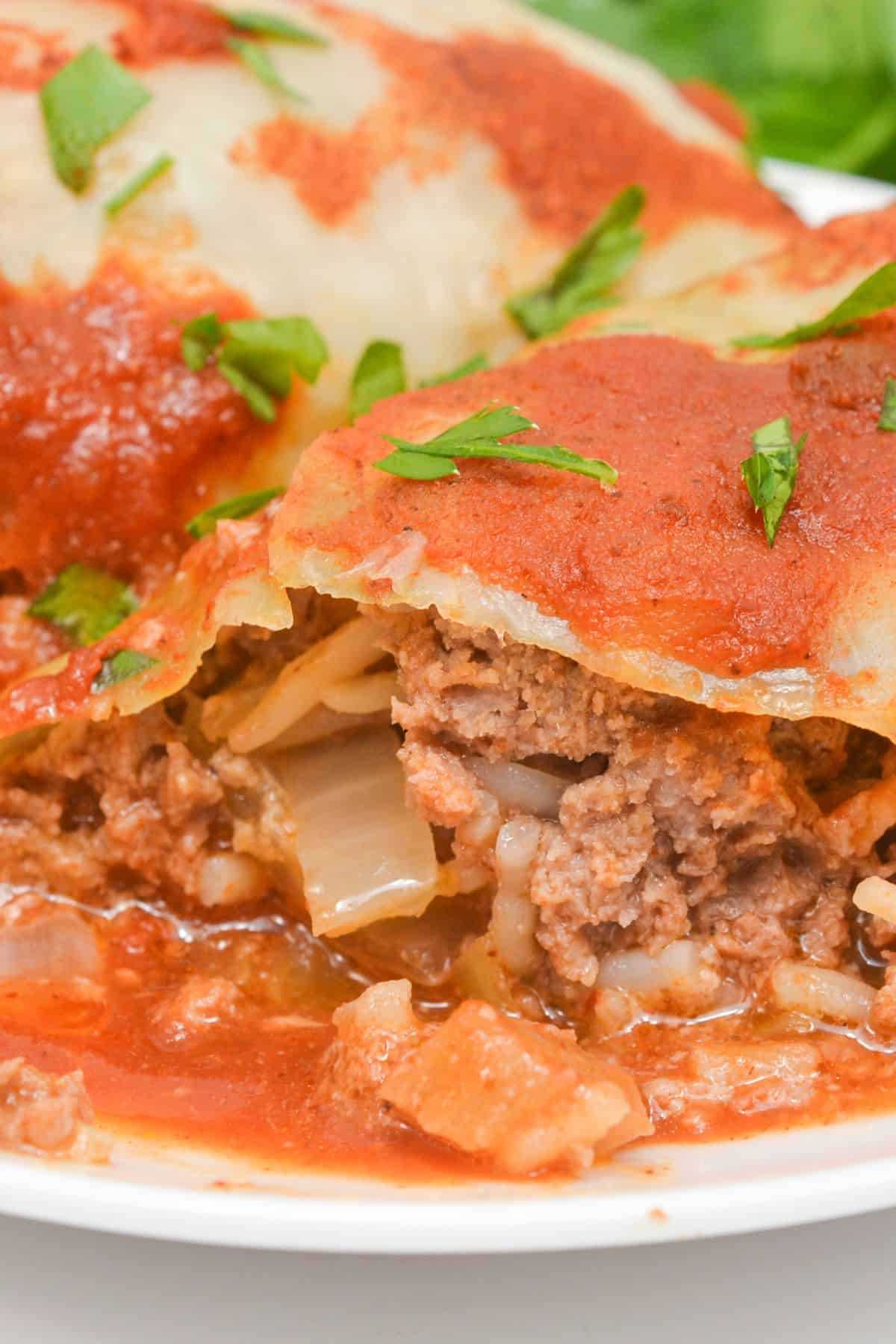 Close-up of Easy Stuffed Cabbage Rolls filled with ground meat, rice, and onions, topped with tomato sauce and garnished with chopped parsley.