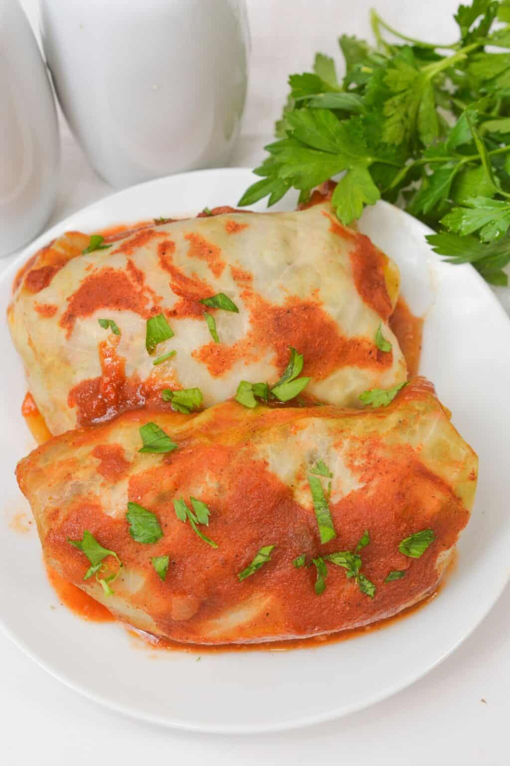Two topped with tomato sauce and chopped parsley are served on a white plate, with fresh parsley in the background.