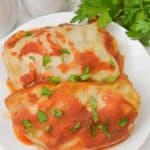 Two topped with tomato sauce and chopped parsley are served on a white plate, with fresh parsley in the background.