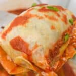 A serving utensil holds up an Easy Stuffed Cabbage Roll, cooked to perfection, covered in red tomato sauce and garnished with chopped herbs.