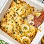 A delicious Potato Bake gratin with sliced potatoes and onions, garnished with parsley, served in a white casserole dish with a wooden spoon.