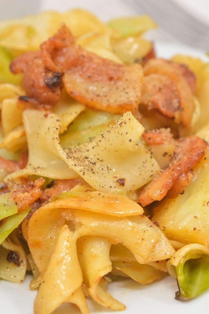 Close-up of a plate of Haluski (Cabbage and Noodles) featuring egg noodles, tender cabbage, and pieces of browned sausage, all seasoned with freshly ground black pepper.
