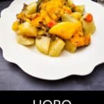 A serving of Hobo Casserole featuring potatoes, ground beef, vegetables, and melted cheese sits on a white scalloped plate.