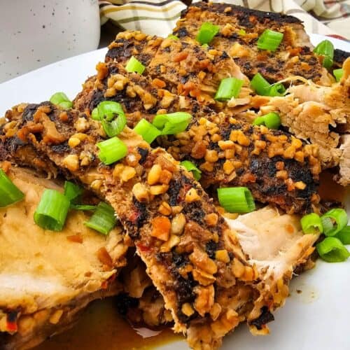 Crock Pot Pork Roast sliced and topped with chopped garlic and green onions on a white plate, with a bowl of rice in the background.