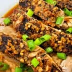 Close-up of Crock Pot Pork Roast, sliced and roasted to perfection, topped with chopped garlic and garnished with green onions on a white plate.
