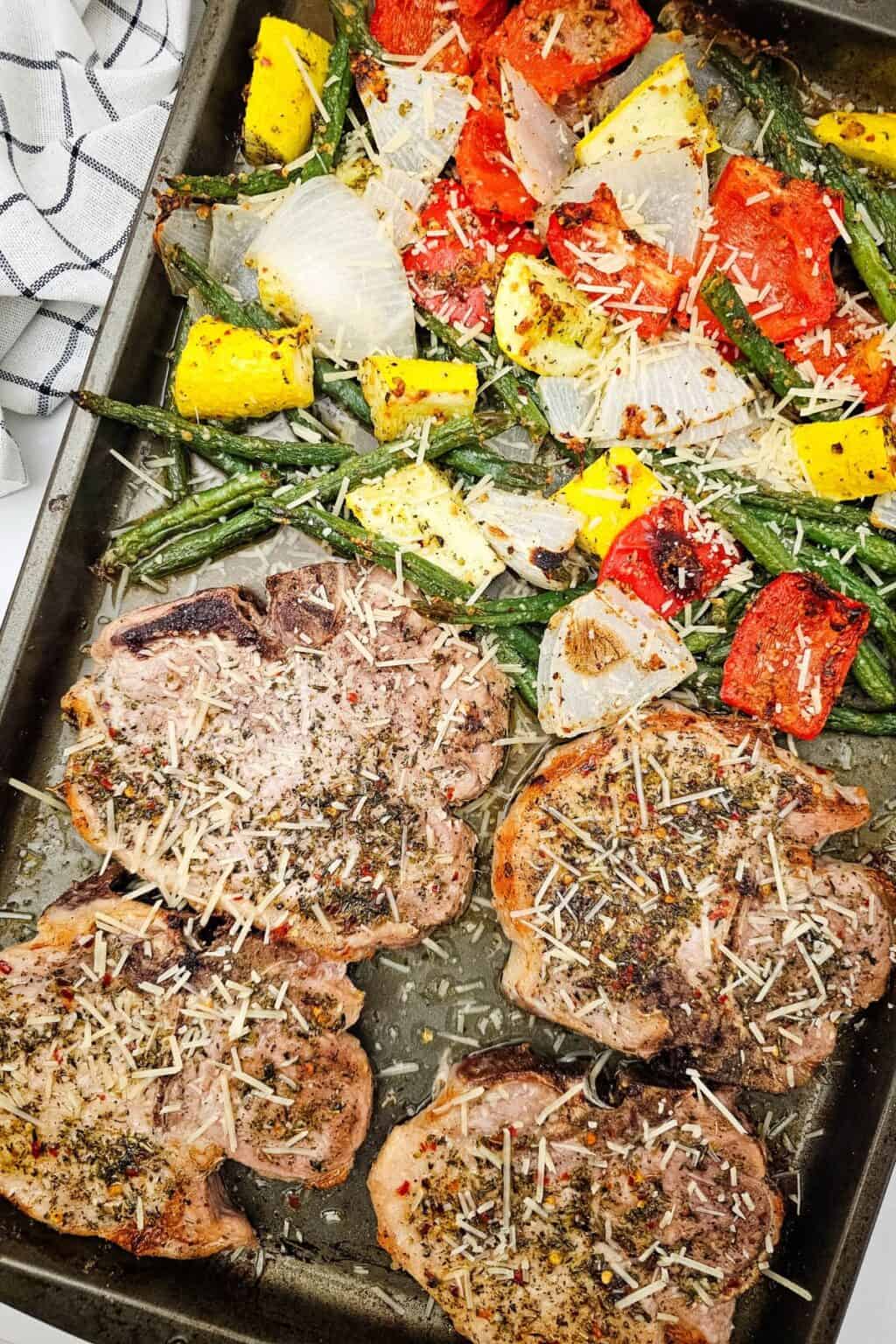 Meat alongside roasted green beans, tomatoes, onions, and yellow squash, all sprinkled with grated cheese for a delicious one-pan meal.