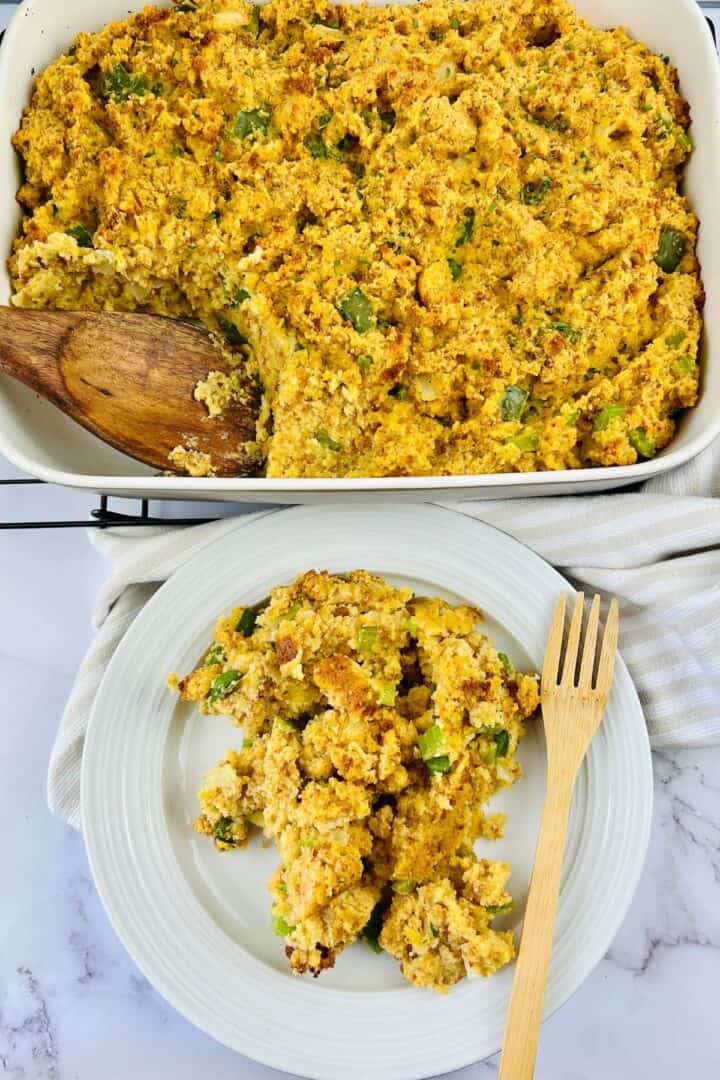 A baking dish of cornbread stuffing with a wooden spoon, and a serving on a white plate with a wooden fork.