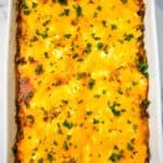 A baked Casserole in a white dish, topped with melted cheddar cheese and chopped parsley.