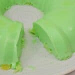 A dessert in a vibrant green ring shape sits on a white plate, with a slice removed to reveal its refreshing, wobbly texture.