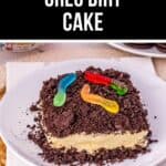 A slice of Oreo Dirt Cake topped with crumbled cookies and gummy worms is served on a white plate, making for a delightfully playful dessert.