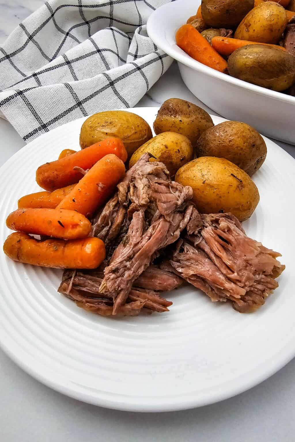 A plate with whole baby potatoes, and cooked carrots, with a bowl of extra potatoes and carrots in the background.