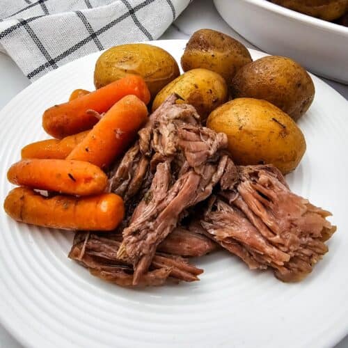 A plate with whole baby potatoes, and cooked carrots, with a bowl of extra potatoes and carrots in the background.