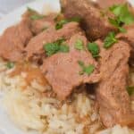 Slow Cooker Beef Tips and Gravy served over white rice, garnished with chopped parsley on a white plate.