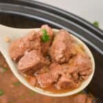 A ladle holds chunks and sauce with herbs, hovered over a pot of the same savory meat.