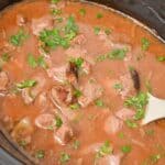 Slow Cooker Beef Tips and Gravy with tender chunks of beef and chopped parsley simmered in a rich brown broth, served right from the slow cooker with a white spoon.